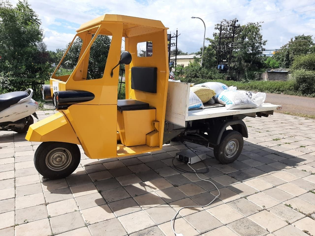 Yellow flatbed variant of Navya parked under trees